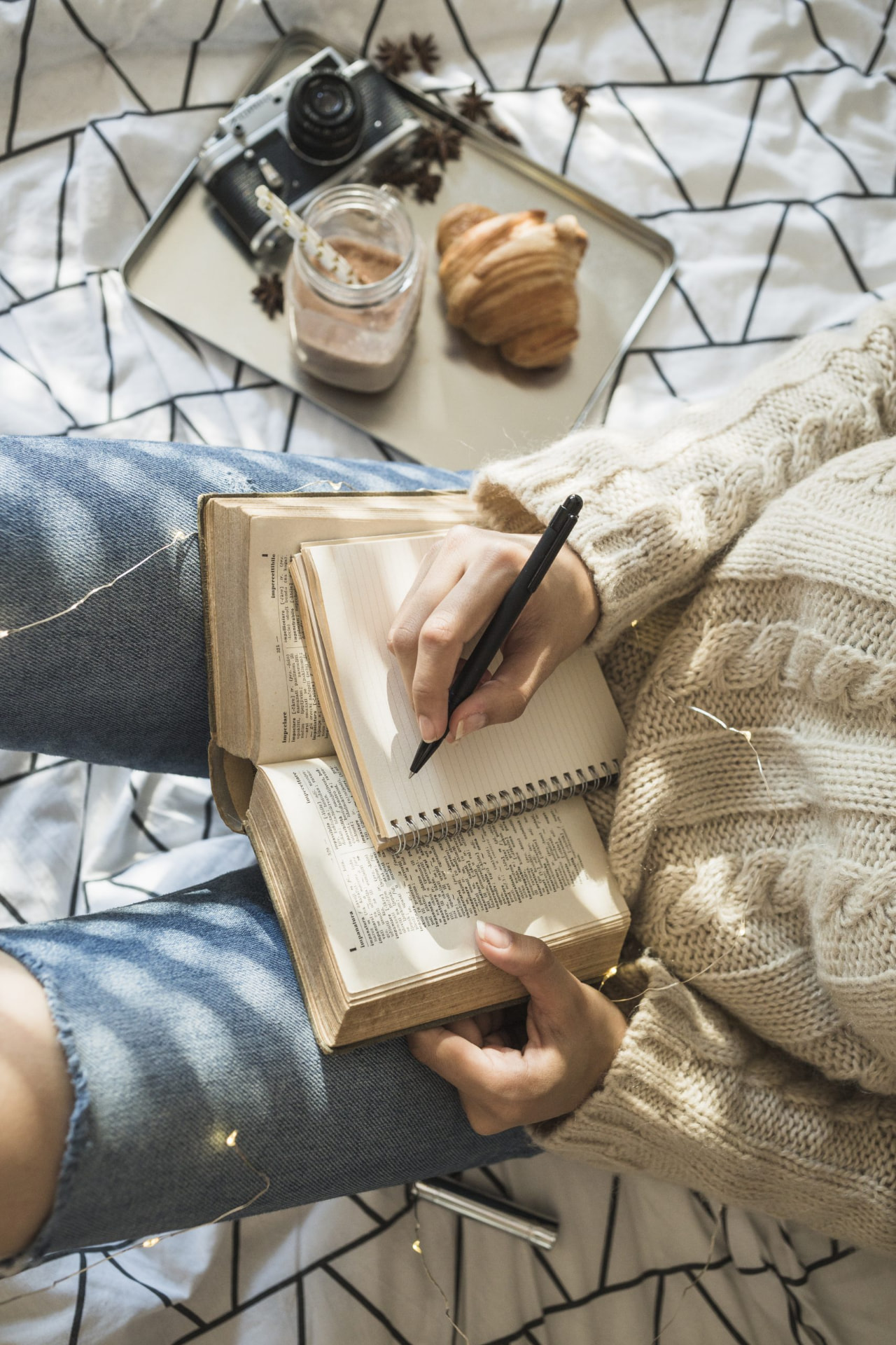A woman journaling beside an open Bible with coffee and fairy lights