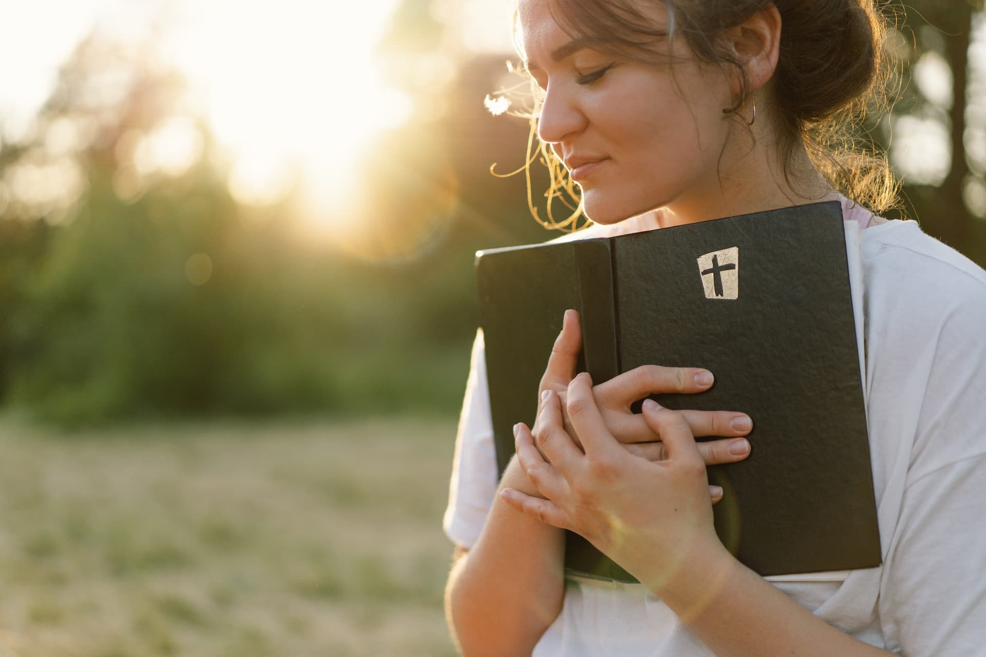 A woman holding a Bible close to her heart at golden hour