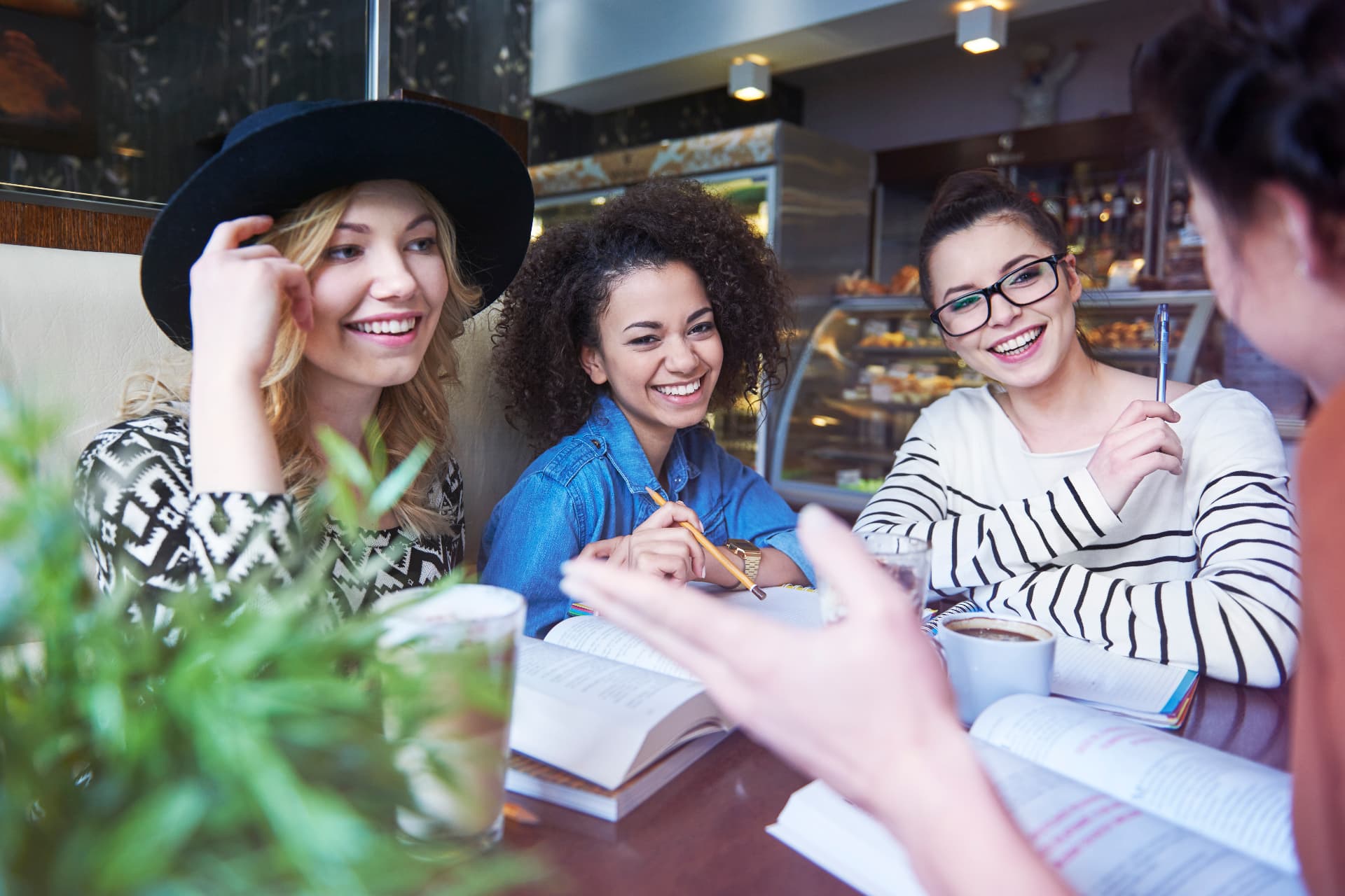 Four women laughing together over coffee and books in a café